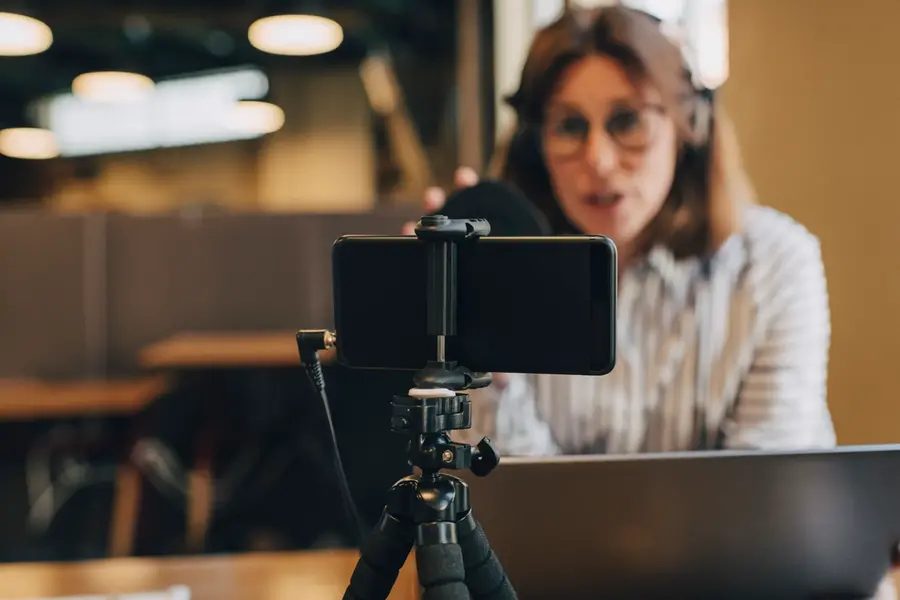 Smarttelefon på stativ som filmar affärskvinna med bärbar dator.